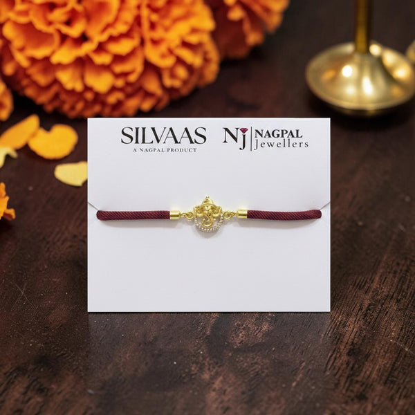 SILVAAS gold-toned Ganesh Ji Rakhi with a maroon thread on a display card, featuring intricate detailing.