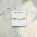 SILVAAS gold-plated Bhai rakhi with a red thread on a branded display card against a white marble background.