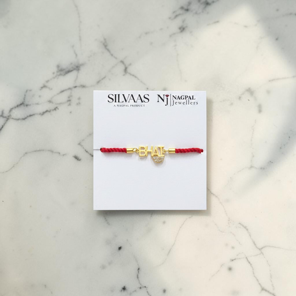 SILVAAS gold-plated Bhai rakhi with a red thread on a branded display card against a white marble background.