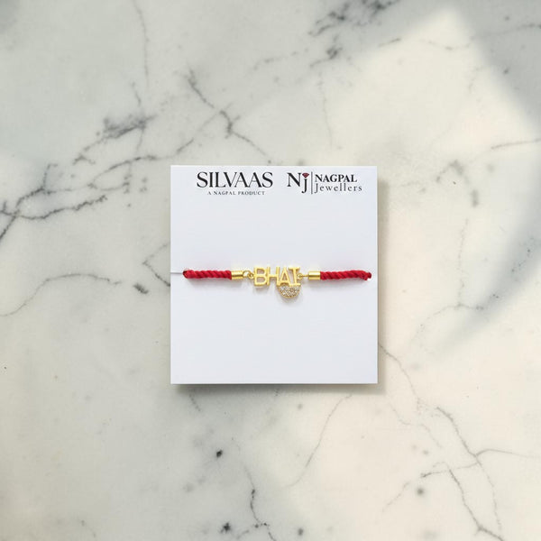 SILVAAS gold-plated Bhai rakhi with a red thread on a branded display card against a white marble background.