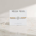 SILVAAS premium silver apple logo Rakhi featuring a stone-encrusted halo on a beige cord, presented on display card.