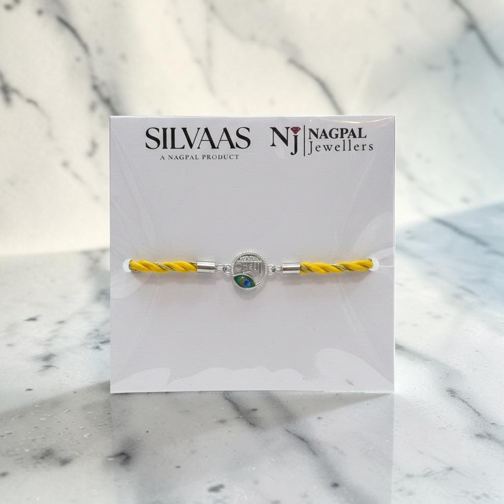 SILVAAS silver Krishna Ji rakhi featuring a circular centerpiece with a peacock feather design on a yellow thread