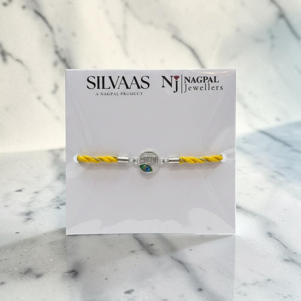 SILVAAS silver Krishna Ji rakhi featuring a circular centerpiece with a peacock feather design on a yellow thread