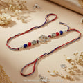SILVAS Om symbol rakhi bracelet with red and blue beads and silver accents on a beige background