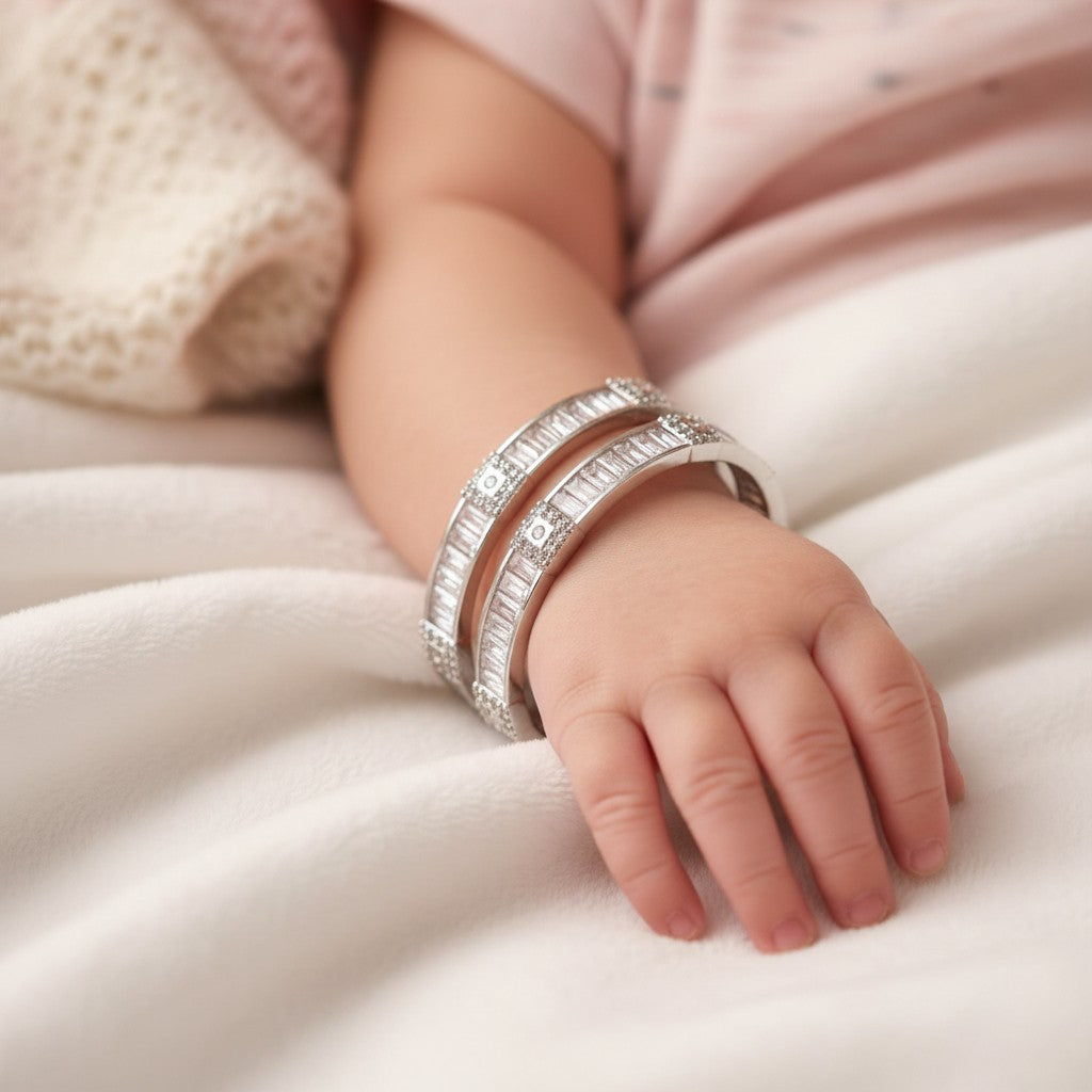 SILVAS silver-tone bangles with baguette-cut cubic zirconia stones worn on a baby's wrist on a soft white blanket.