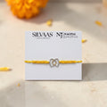 SILVAS 92.5 sterling silver BRO rakhi with a yellow thread on a branded display card