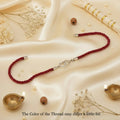 SILVAS sterling silver heart Rakhi with red braided thread on a cream satin background with decorative diyas