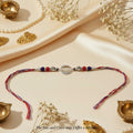 SILVAS 92.5 sterling silver Om symbol Rakhi with red and blue beads on a multi-colored thread, festive flat lay.