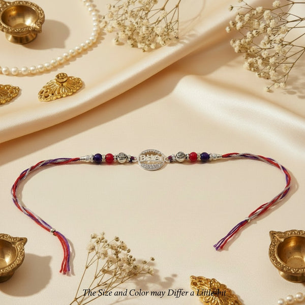 SILVAS 92.5 sterling silver Om symbol Rakhi with red and blue beads on a multi-colored thread, festive flat lay.