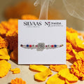 SILVAS 92.5 sterling silver Swastika rakhi with red and blue beads on a vibrant thread, presented on a display card.